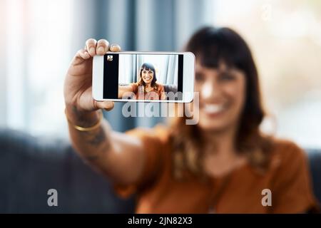 Es ist einfach so verlockend, Selfies zu machen. Eine junge Frau, die Selfies macht, während sie sich zu Hause entspannt. Stockfoto
