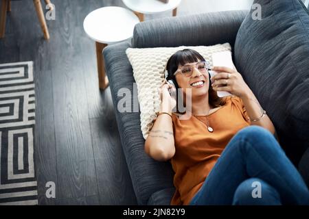 Dies ist meine Lieblings-Wiedergabeliste. Eine junge Frau, die Kopfhörer trägt, während sie sich zu Hause entspannt. Stockfoto