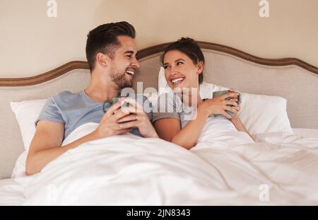 Ein glückliches junges Paar, das zu Hause im Schlafzimmer Kaffee im Bett trank. Stockfoto