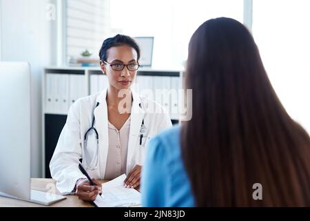 Das Zuhören ist ein wichtiger Teil des Diagnoseprozesses. Eine junge Ärztin führt ein Gespräch mit einer Patientin in ihrem Sprechzimmer. Stockfoto
