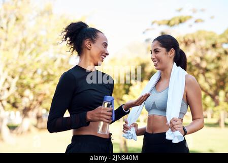 Nehmen wir eine kurze Pause. Zwei attraktive junge Frauen lächeln sich nach ihrem Lauf im Park tagsüber an. Stockfoto