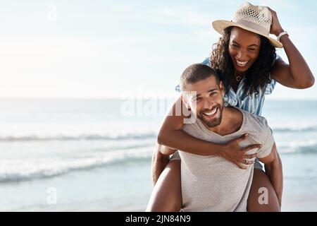 Wir haben einfach unseren Tag in der Sonne geliebt. Porträt eines jungen Mannes, der seine Freundin am Strand mit Huckepack zurückkickt. Stockfoto