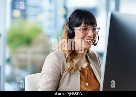 Ich habe die Informationen gefunden, die Sie suchen: Eine attraktive junge Geschäftsfrau, die tagsüber in ihrem Büro sitzt und ein Headset benutzt. Stockfoto