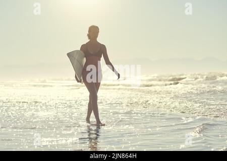 Ich glaube, ich kann fliegen wie jeder Surfer. Eine junge Frau mit ihrem Surfbrett am Strand. Stockfoto