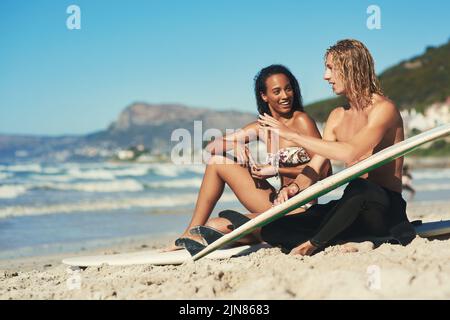 Wir lernten, mit dem Fluss zu gehen. Ein junges Paar, das mit ihren Surfbrettern am Strand saß. Stockfoto