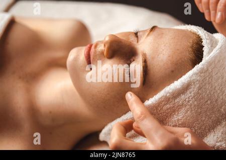 Kaukasische Sommersprossen-Frau mit Gesichtsmassage in einem Spa-Salon. Schönheitsbehandlung. Attraktive elegante Frau. Spa-Behandlung. Stockfoto