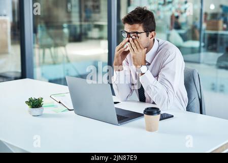 Arbeitsstress kommt zu ihm. Ein Geschäftsmann, der gestresst aussieht, während er an seinem Schreibtisch sitzt. Stockfoto
