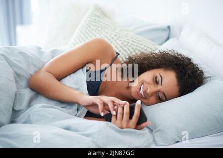 Das ist so ein lustiger Text. Eine attraktive junge Frau, die auf ihrer Seite im Bett liegt und morgens ihr Handy benutzt. Stockfoto