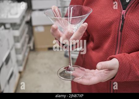 Das kaukasische Mädchen kauft im Geschäft großes, transparentes Glas für Martinis und Cocktails Stockfoto