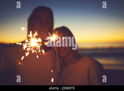 Beleuchten Sie die Nacht mit etwas Magie. Ein junges Paar spielt mit Wunderkerzen am Strand in der Nacht. Stockfoto