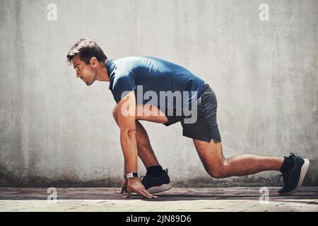 Setzen Sie sich auf ein neues Sie. Ein sportlicher junger Mann in Ausgangsposition beim Training im Freien. Stockfoto