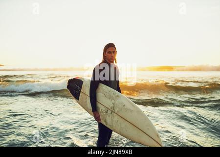 Es ist etwas Cooles, sich selbst als Surfer zu bezeichnen. Porträt eines jungen Mannes, der ein Surfbrett am Strand trägt. Stockfoto