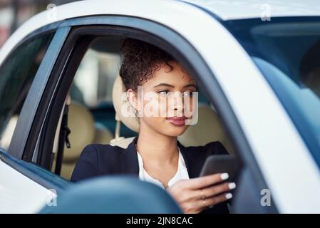 Eine attraktive junge Geschäftsfrau, die ein Smartphone benutzt, während sie in ihrem Auto sitzt. Stockfoto