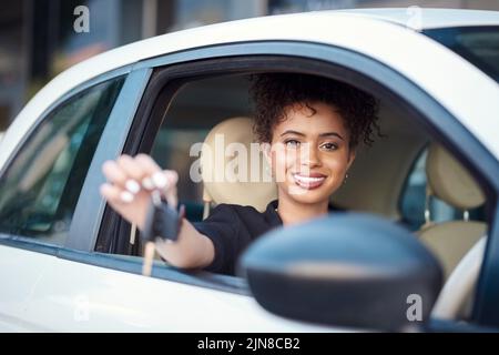 Shes offiziell ein Autobesitzer. Ein Porträt einer attraktiven jungen Geschäftsfrau, die ihre Autoschlüssel hochhält, während sie in ihrem neuen Auto sitzt. Stockfoto
