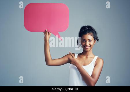Machen Sie Ihre Stimme hörbar. Studioporträt einer schönen jungen Frau, die ein leeres Schild vor einem grauen Hintergrund hochhält. Stockfoto