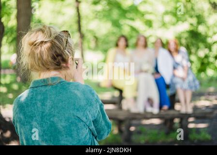 Ein Hochzeitsfotograf fotografiert die Gäste des Brautpaares an einem sonnigen Tag in der Natur Stockfoto