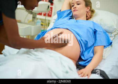 Du und das Baby machen es bisher großartig. Eine junge Schwangere wird von einem Arzt untersucht, während sie in ihrem Krankenhausbett liegt. Stockfoto