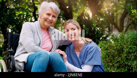 Sie ist immer an meiner Seite. Eine fröhliche ältere Frau im Rollstuhl verbringt Zeit mit ihrer Tochter draußen in einem Park. Stockfoto