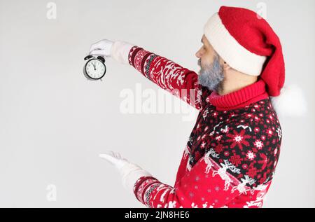 Weihnachts- und Weihnachtskonzept. Der Weihnachtsmann zeigt auf die Uhr vor Weihnachten. Weihnachtsmütze auf der Uhr Stockfoto