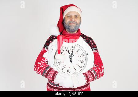 Weihnachts- und Weihnachtskonzept. Der Weihnachtsmann zeigt auf die Uhr vor Weihnachten. Weihnachtsmütze auf der Uhr Stockfoto