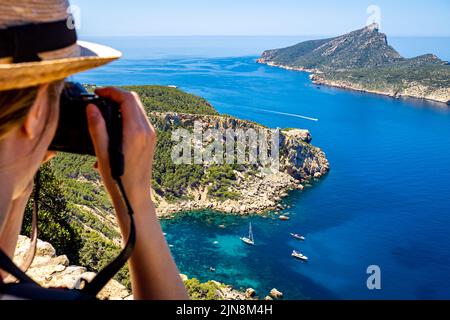 Rückansicht einer jungen weißen Frau mit Kamera und Hut über der gemütlichen Bucht Cala en Basset in der Nähe des Dorfes Sant Elm an der westlichsten Seite Mallorcas Stockfoto