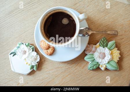 Tasse heißen aromatisierten schwarzen Kaffee mit weichem Schaum auf der Untertasse und schöne Puderblume geformten Cookies auf dem Tisch Draufsicht Nahaufnahme, freie Kopie Platz. Catering Stockfoto