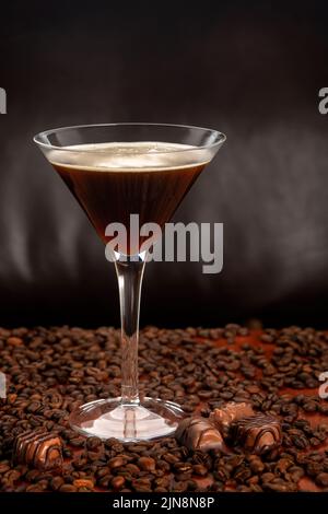 Espesso Martini-Cocktail in einem martini-Glas auf einer Basis mit Schokolade und Kaffeebohnen vor dunklem Hintergrund Stockfoto