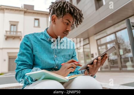 Typ, der auf das Tablet mit Notizblock und Stift sitzt Stockfoto