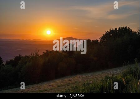 Sonnenuntergang über Bergen, Wald und Wiese, Hügel Jested am Horizont, Abend auf Hügel Kozakov, Tschechische Paradies, Tschechische republik. Stockfoto