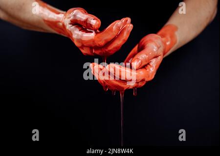 Frauenhände in einer zähflüssigen roten Flüssigkeit ähnlich dem Blut. Stockfoto