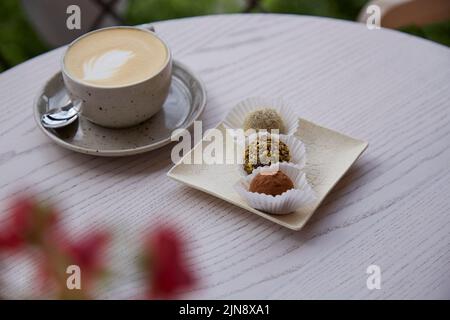 Natürliche vegane Trüffel ohne Mehl, Milch und Backwaren sowie eine Tasse Cappuccino auf einem Holztisch im Freien auf der Café-Terrasse. Kaffeepause Stockfoto