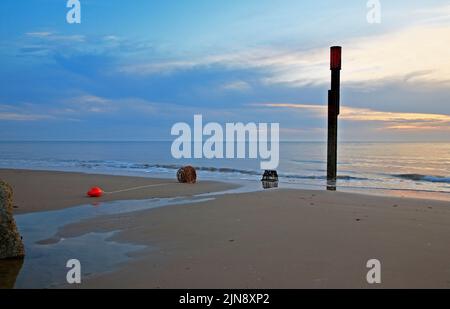 Ein Blick am frühen Morgen auf den Strand und das Meer im Sommer mit gebrannten Hummertöpfen und roter Boje in Happisburgh, Norfolk, England, Großbritannien. Stockfoto