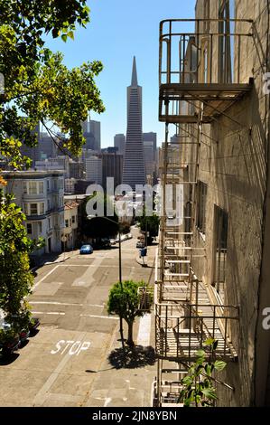 San Francisco an einem sonnigen Tag Hinterstraße und Metall-Stufen der Feuertreppe aus dem Wohnhaus mit hohen Stadtgebäuden in der Ferne. Groß. Stockfoto