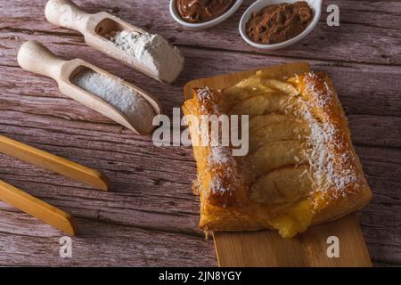 Nahaufnahme eines mit Schokolade überzogenen Blätterteigs mit Creme und Mandeln auf einem weißen Teller auf dunklem Hintergrund Stockfoto