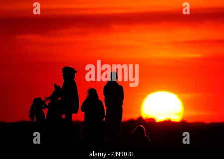 Gruppen von Menschen beobachten den Sonnenuntergang von einem Hügel in Ealing, West-London, während ein Sommer voller Rohrleitungsverbote und Feuerwarnungen anhält, wobei in weiten Teilen des Landes ein Wärmestandalarm ausgelöst wird. Bilddatum: Dienstag, 9. August 2022. Stockfoto