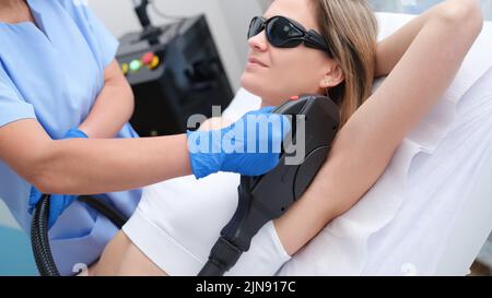 Frau durchläuft Haarentfernungsverfahren mit Photoepilator oder Laser-Haarentfernung von Achselhöhlen im Salon Stockfoto