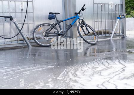 Waschen eines Fahrrads mit einem Schaumstrahl bei einer Autowäsche. Das Fahrrad ist mit Schaumstoff überzogen. Self-Service. Fahrradwartung. Stockfoto