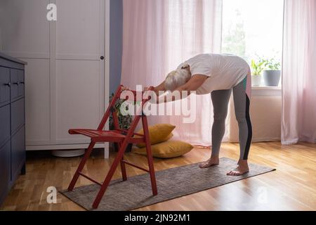 Reife Frau in legerer Kleidung zu Hause trainieren, Yoga üben Stockfoto