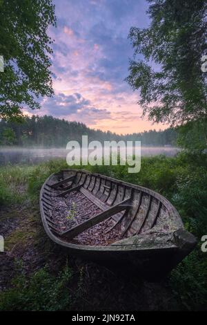 Schöner Sonnenaufgang in einem ruhigen See am Sommerabend in Finnland mit einem Holzboot Stockfoto