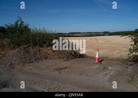 Marlow Bottom, Buckinghamshire, Großbritannien. 10.. August 2022. Der Zugang für Feuerwehrfahrzeuge wurde durch eine Hecke geBulldosiert. Die Folgen eines riesigen Feuers Anfang dieser Woche. Etwa zwei Hektar geschnittenes Stroh, Hecken, Sträucher und Zäune auf einer Farm wurden durch das Feuer auf dem Ackerland neben einem öffentlichen Fußweg vor der Ragmans Lane zerstört. Buchenholzknödel mit Kunststoffabdeckungen um sie herum entlang des Fußweges lagen geschmolzen und geschwärzt. Quelle: Maureen McLean/Alamy Live News Stockfoto