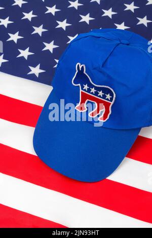 Blaue DNC-Kappe mit dem Esel-Emblem und US Stars and Stripes Flagge. Für die Präsidentschaftswahlen 2024 in den USA und die Vernichtung der Demokraten durch die republikanische Rote Welle. Stockfoto