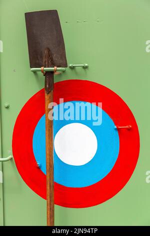 Spaten, der an der Seite eines alten Militärfahrzeugs angebracht ist, neben einer rot-blau-weißen Kakade. Stockfoto