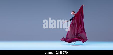 Porträt der jungen Ballerina tanzen bedeckt mit tiefrotem transparentem Stoff isoliert über blau grauen Studio-Hintergrund. Stockfoto