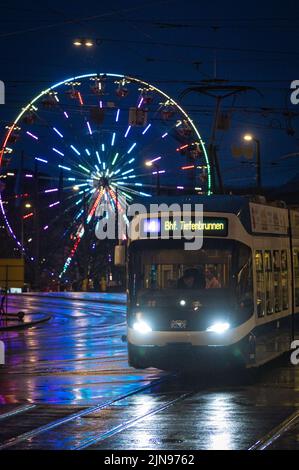 Eine vertikale Aufnahme einer Straßenbahn mit einem Riesenrad im Hintergrund in einer regnerischen Nacht. Zürich, Schweiz. Stockfoto