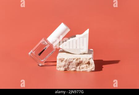 Wiederfüllbare Flasche aus klarem Glas mit Bürstendeckel in der Nähe beigefarbener Travertin-Steine auf rosa, Nahaufnahme, Mockup. Hautpflege Nagel Produkt. Naturkosmetik, minimal Stockfoto