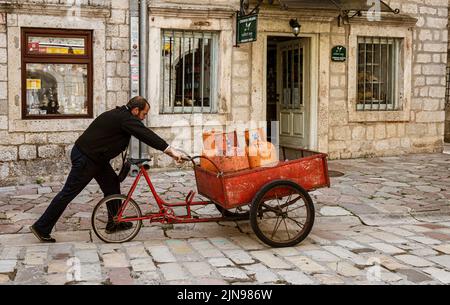 Montenegro - 7. Mai 2022 - Mann schiebt Dreirad mit Propan Tanks für Häuser. Stockfoto