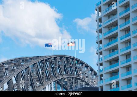 Von Kirribilli aus gesehen, fliegt die Flagge der Aborigines mit starkem Westwind nun neben der australischen Flagge über der Sydney Harbour Bridge Stockfoto