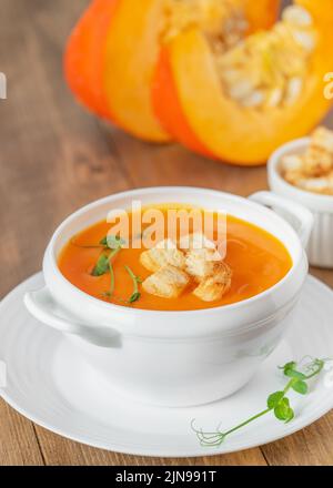 Kürbissuppe mit Croutons in weißer Schale auf Holzgrund. Nahaufnahme Stockfoto