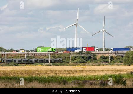 Stafford-Staffordshire-Vereinigtes Königreich 27. April 2022 grünes Sumpfland grenzt an eine verkehrsreiche Autobahn und Bahnlinie mit zwei Windenergieanlagen, Stockfoto