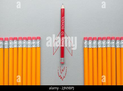 Zurück zur Schule roter Bleistift mit Raketenskizze, der sich zwischen einer Reihe orangefarbener Bleistifte heraussticht Stockfoto